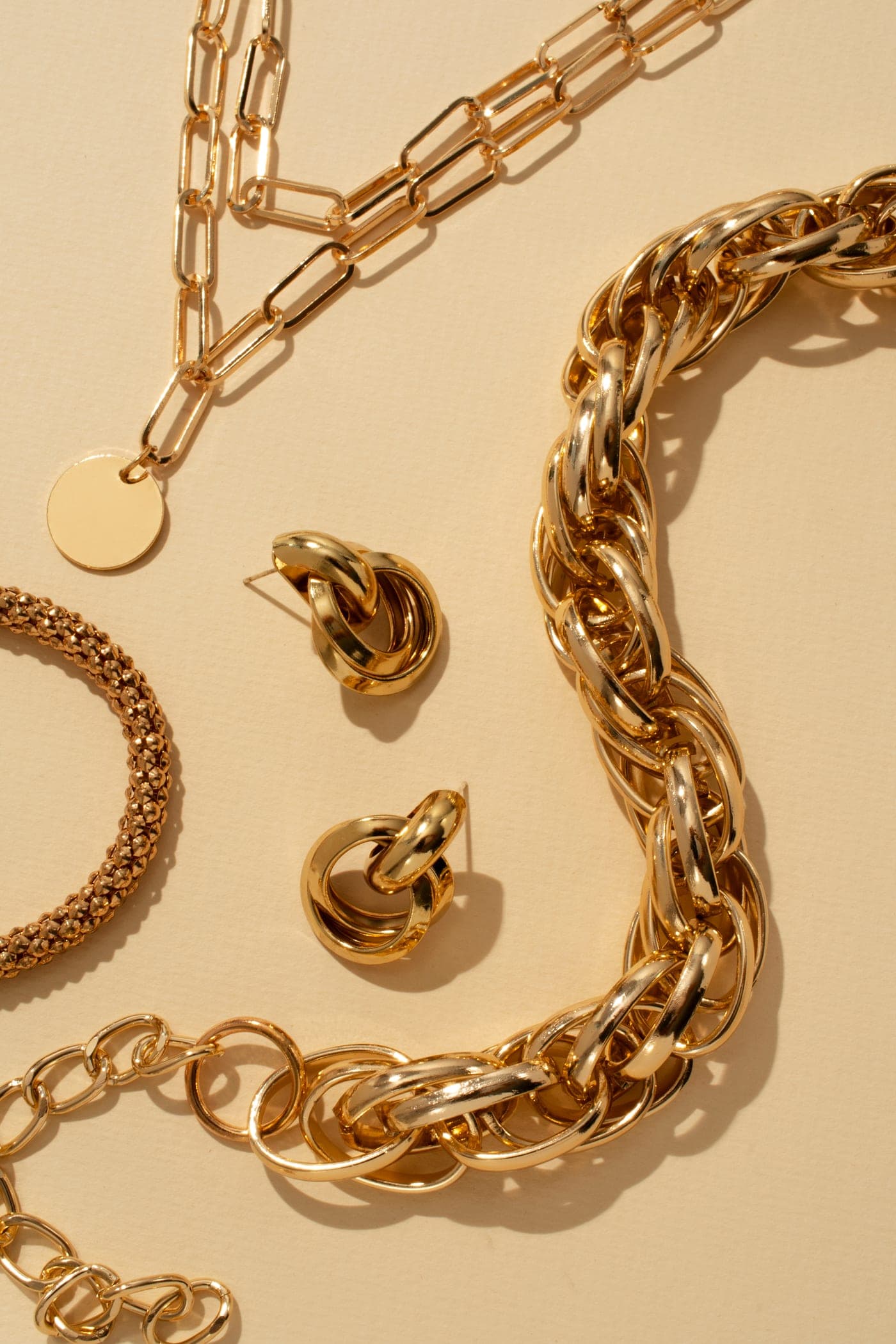 Bold gold chains and earrings arranged on cream