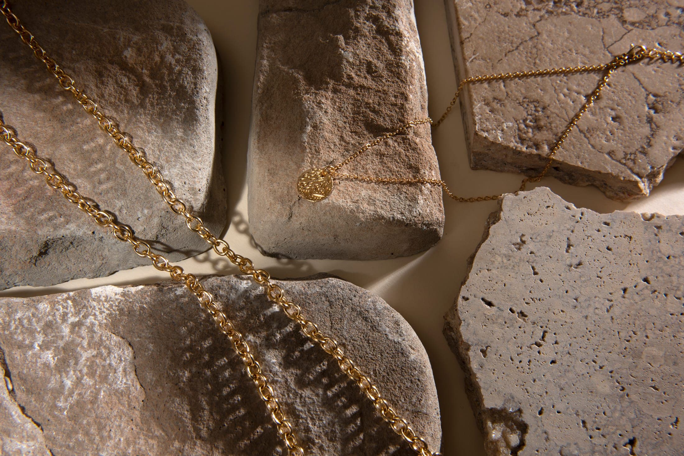 Gold chains and pendants draped over warm stone